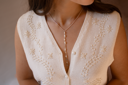 Woman wearing a white embroidered vest with a necklace against a neutral background