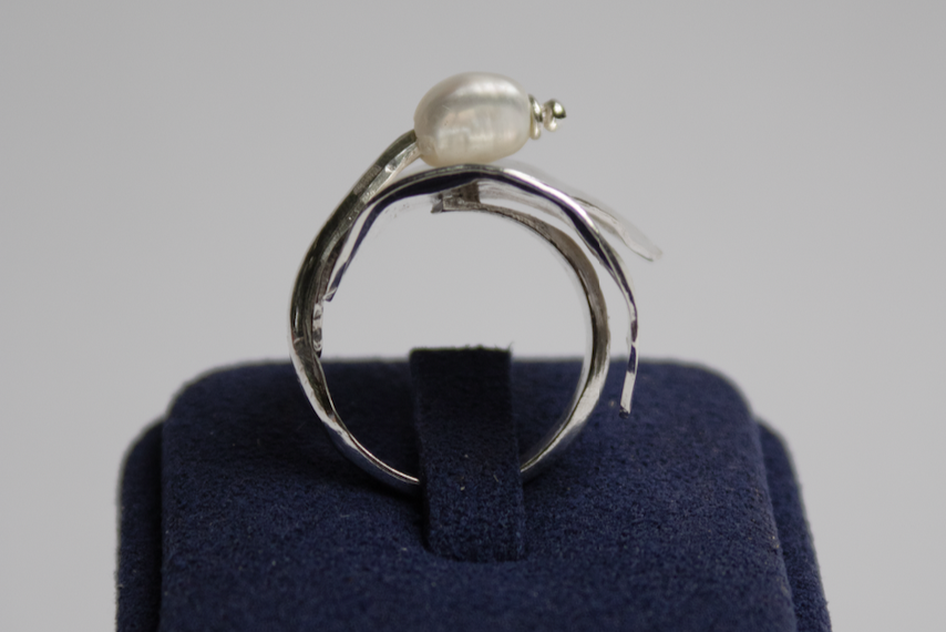 Silver ring with a pearl on a blue cushion against a gray background