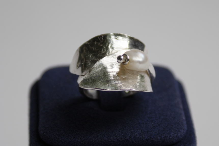 Silver ring on a dark blue cushion with a plain background