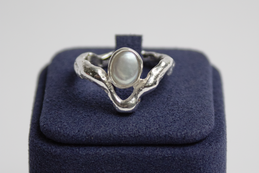 Silver ring with a pearl on a blue box against a light gray background