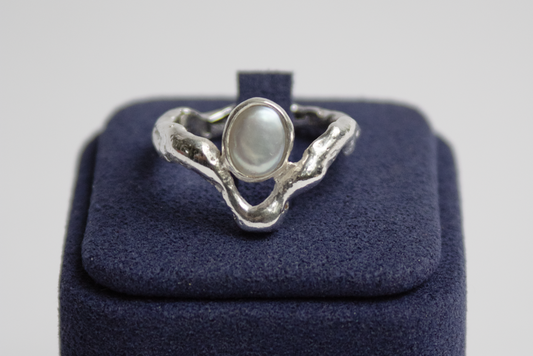 Silver ring with a pearl on a blue box against a light gray background